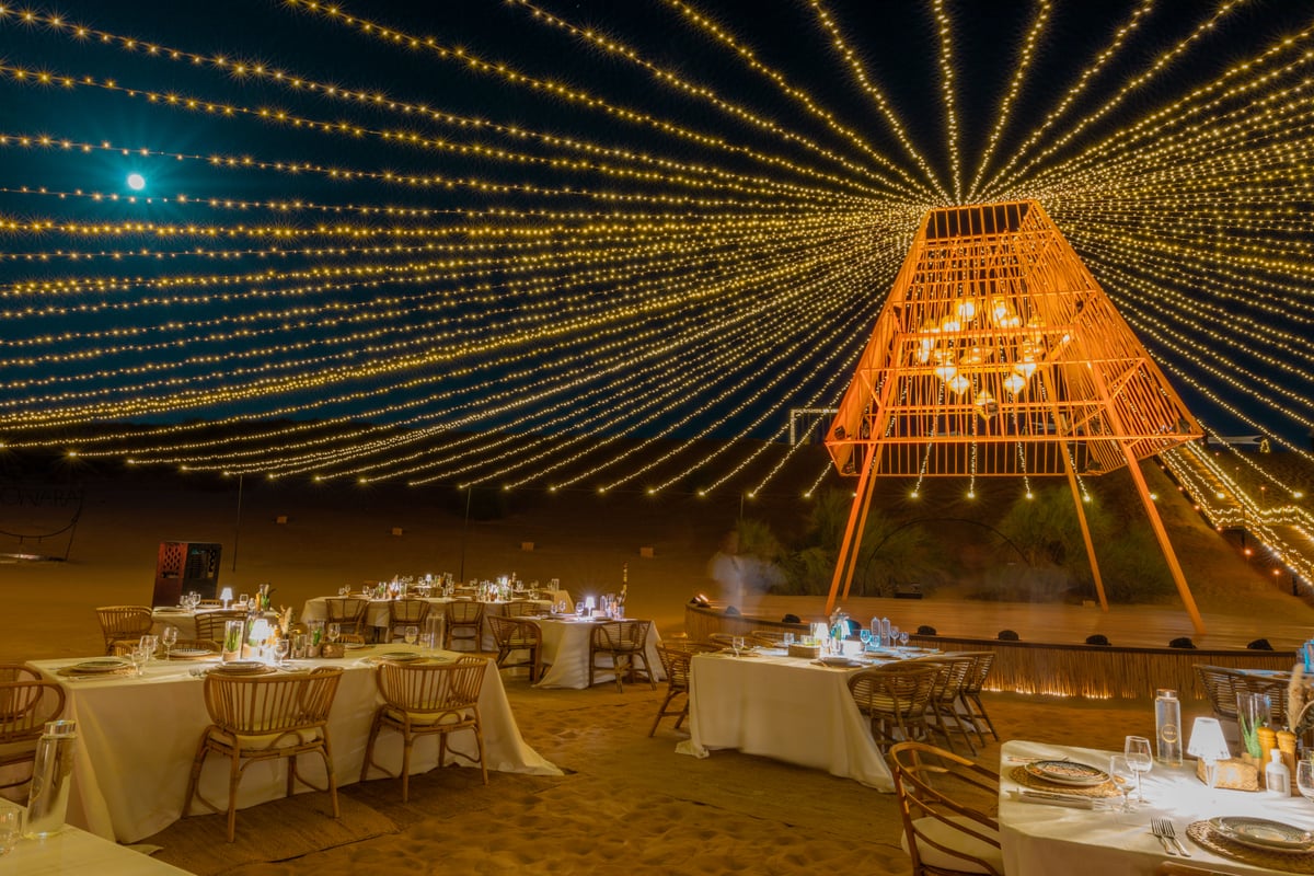 Tables laid for dinner under a canopy of fairy lights and a lit rattan tower