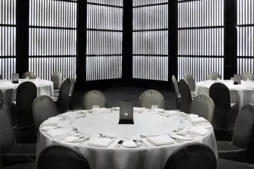 Round dinner tables laid in white under tall slatted windows in the Armani Hotel ballroom