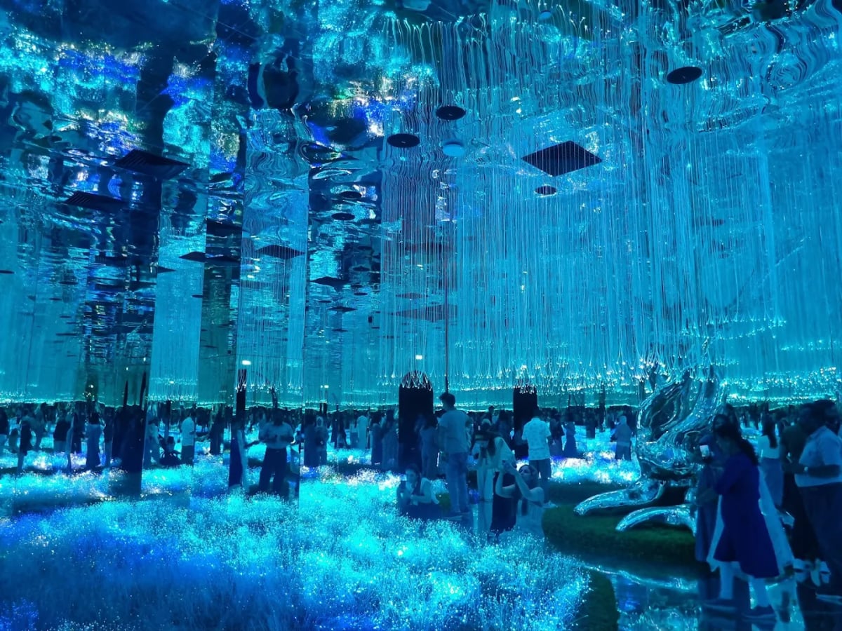 Visitors among curtains of blue light threads around a silver sculpture