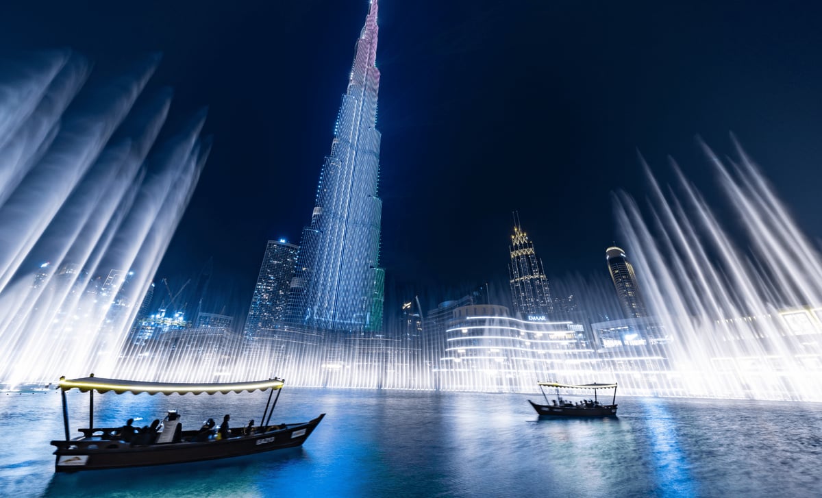 Passengers in a traditional abra on the lake as fountain jets fan out beneath Burj Khalifa at night