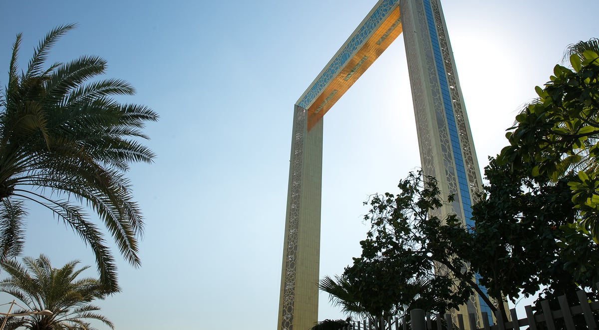 The gold Dubai Frame rising above palm trees in Zabeel Park on a bright morning