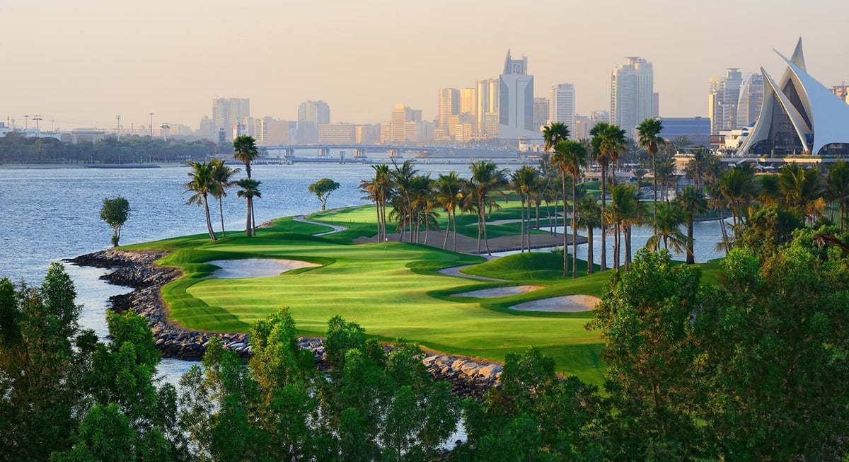 A green framed by palms and water at Dubai Creek, the city skyline behind