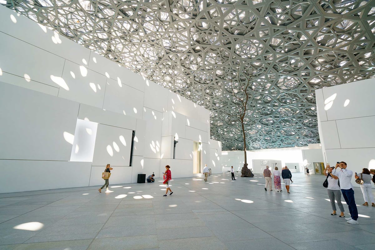 Visitors walking beneath the latticed dome as dappled sunlight falls on white galleries
