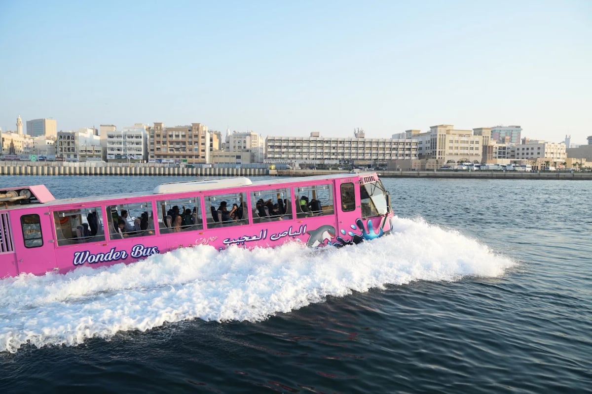 A pink amphibious Wonder Bus speeding across Dubai Creek