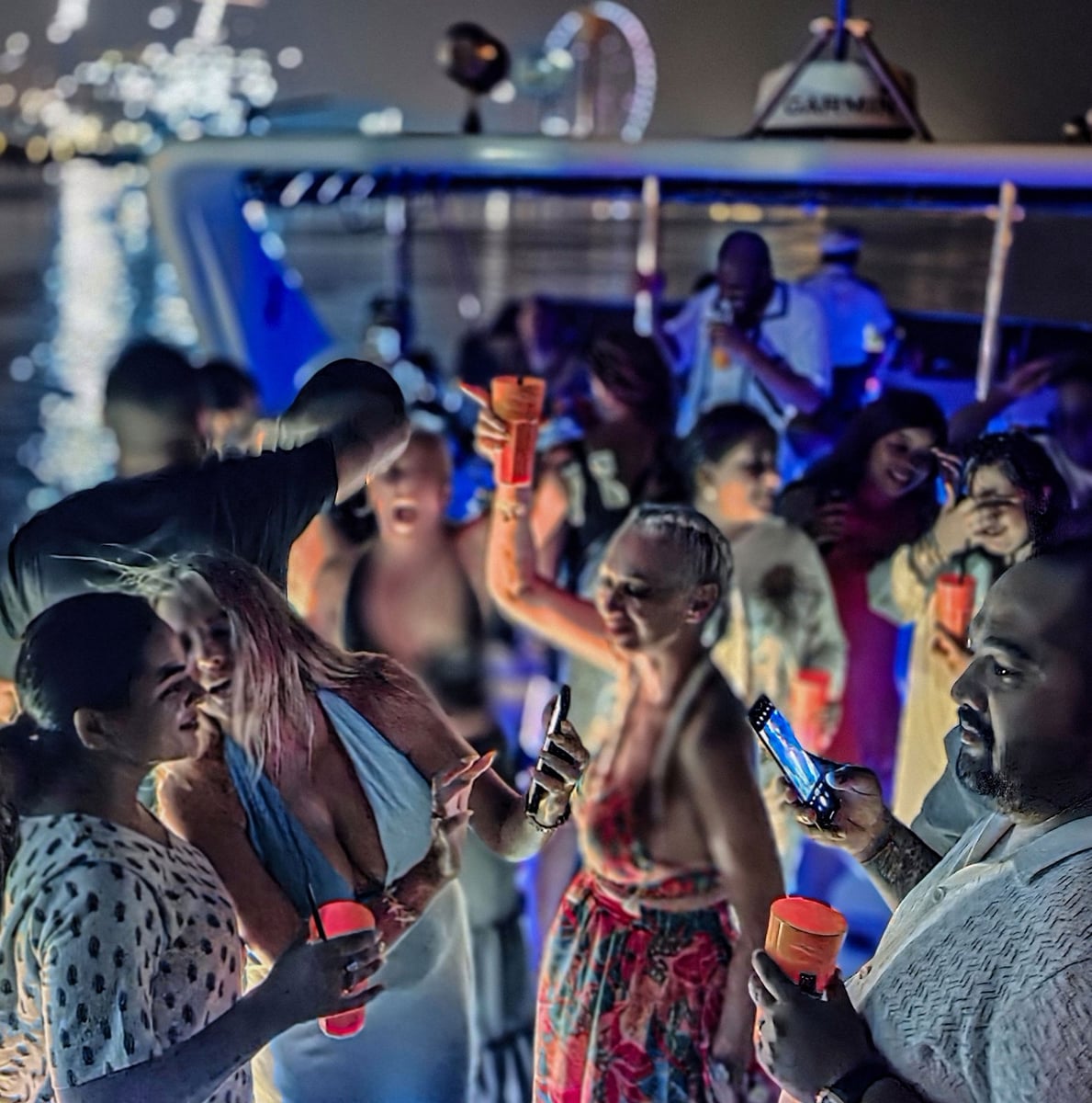 A crowd dancing on a yacht's deck at night with Ain Dubai lit behind