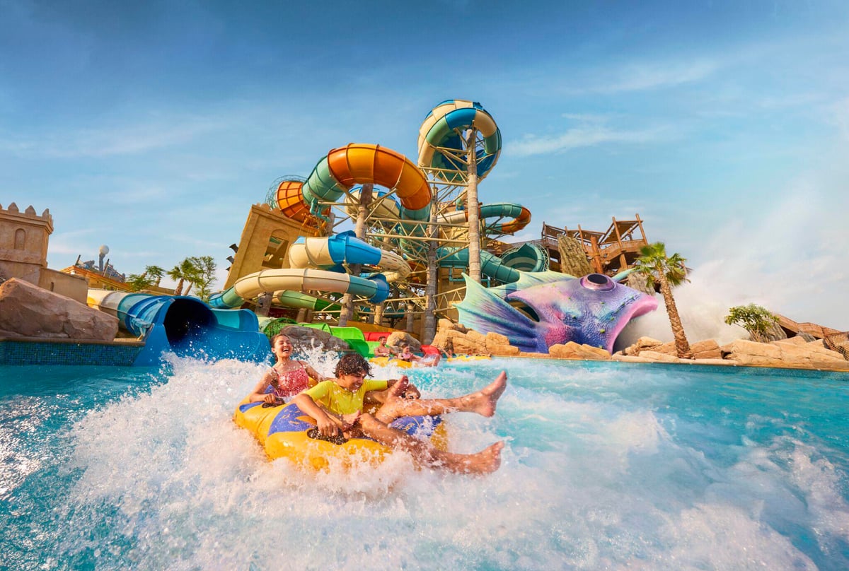 A tube of riders splashing down in front of the park's tall slide towers on a sunny day