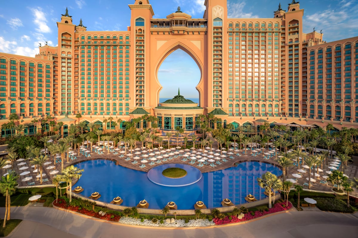 The curved main pool at Atlantis The Palm seen from above, ringed by rows of umbrellas in front of the arch.