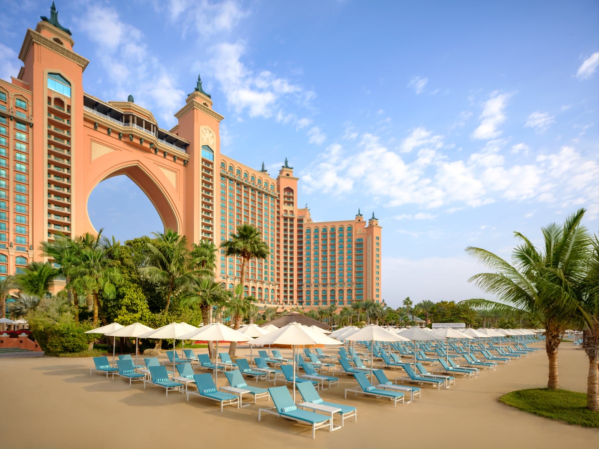 Rows of blue loungers and white umbrellas on the main beach at Atlantis The Palm, with the arch behind.