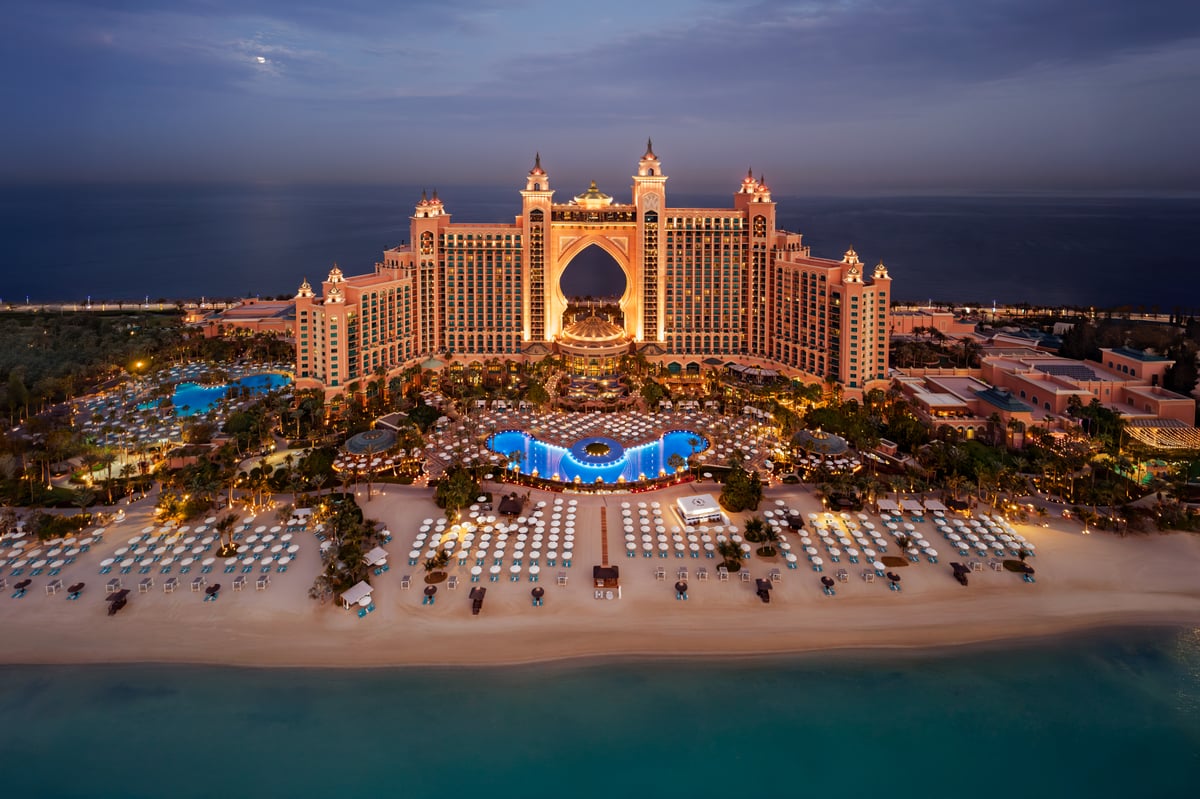 Atlantis The Palm lit up at night, seen from above the beach with the illuminated pool and gardens in front.