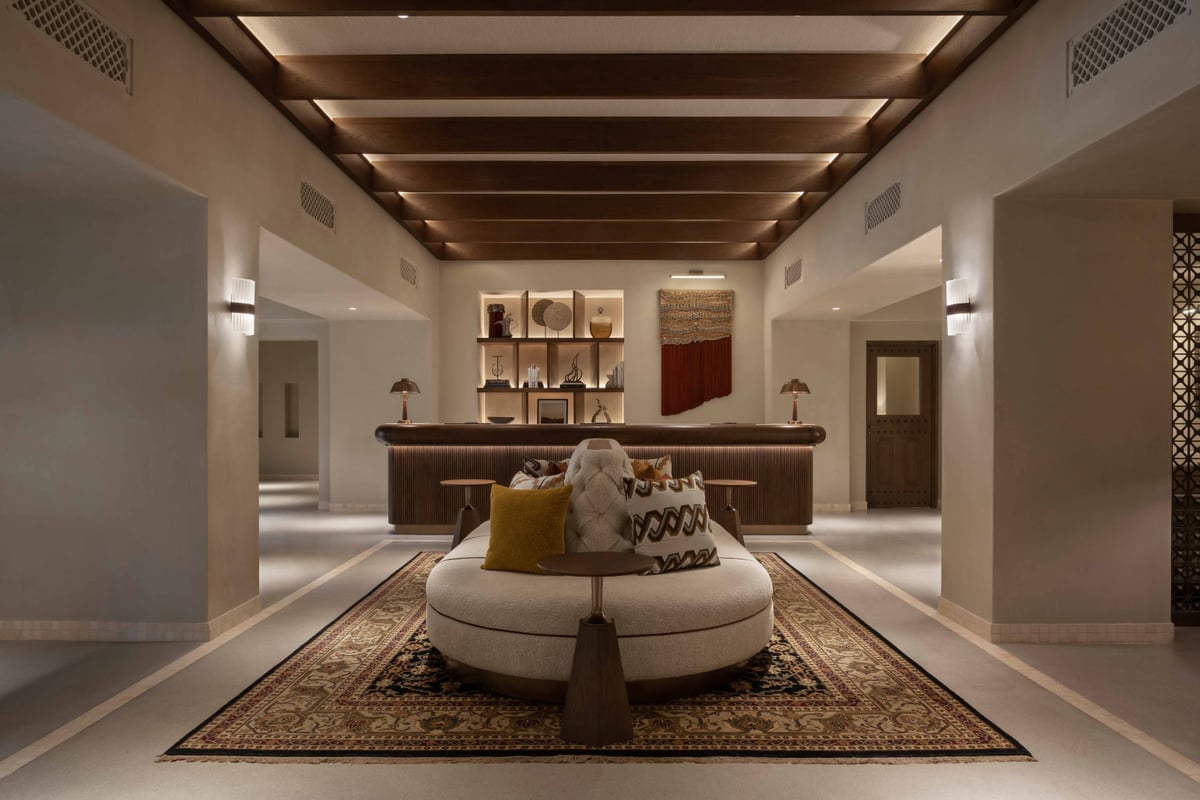 The reception at Bab Al Shams with a round sofa on a patterned rug, a wooden ceiling and a long desk.