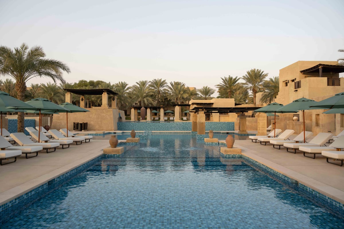 A long pool at Bab Al Shams edged with sun loungers, green parasols and palm trees.