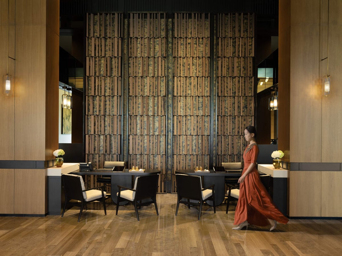 A woman in a long dress walks past the wood-screened reception lounge of Banyan Tree Dubai.