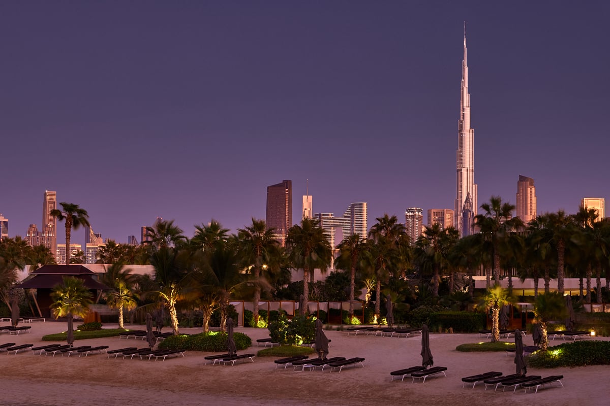 Palm trees and lit loungers on the Bvlgari Resort Dubai beach at night, the Burj Khalifa and downtown towers behind.