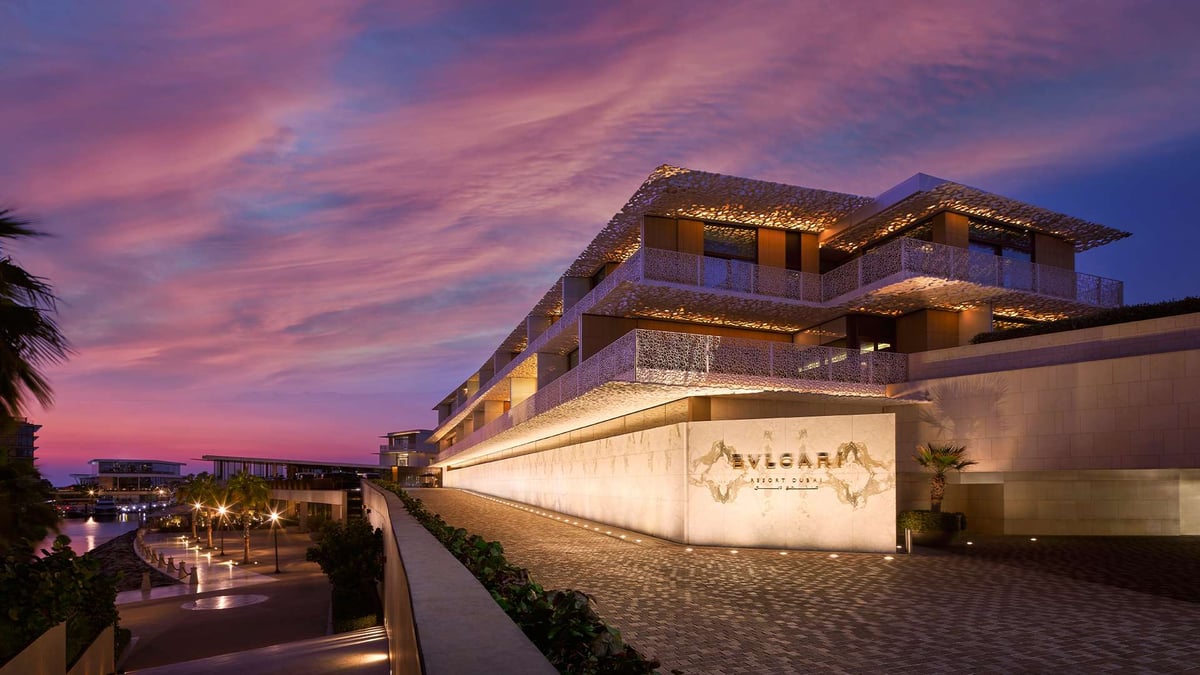 The Bvlgari Resort Dubai entrance at dusk, lit stone walls and terraced floors under a pink and violet sky.