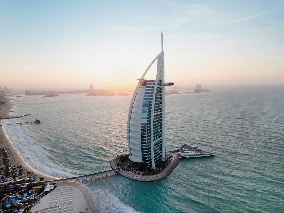 Burj Al Arab's sail-shaped tower on its island, linked to the shore by a bridge, at sunset