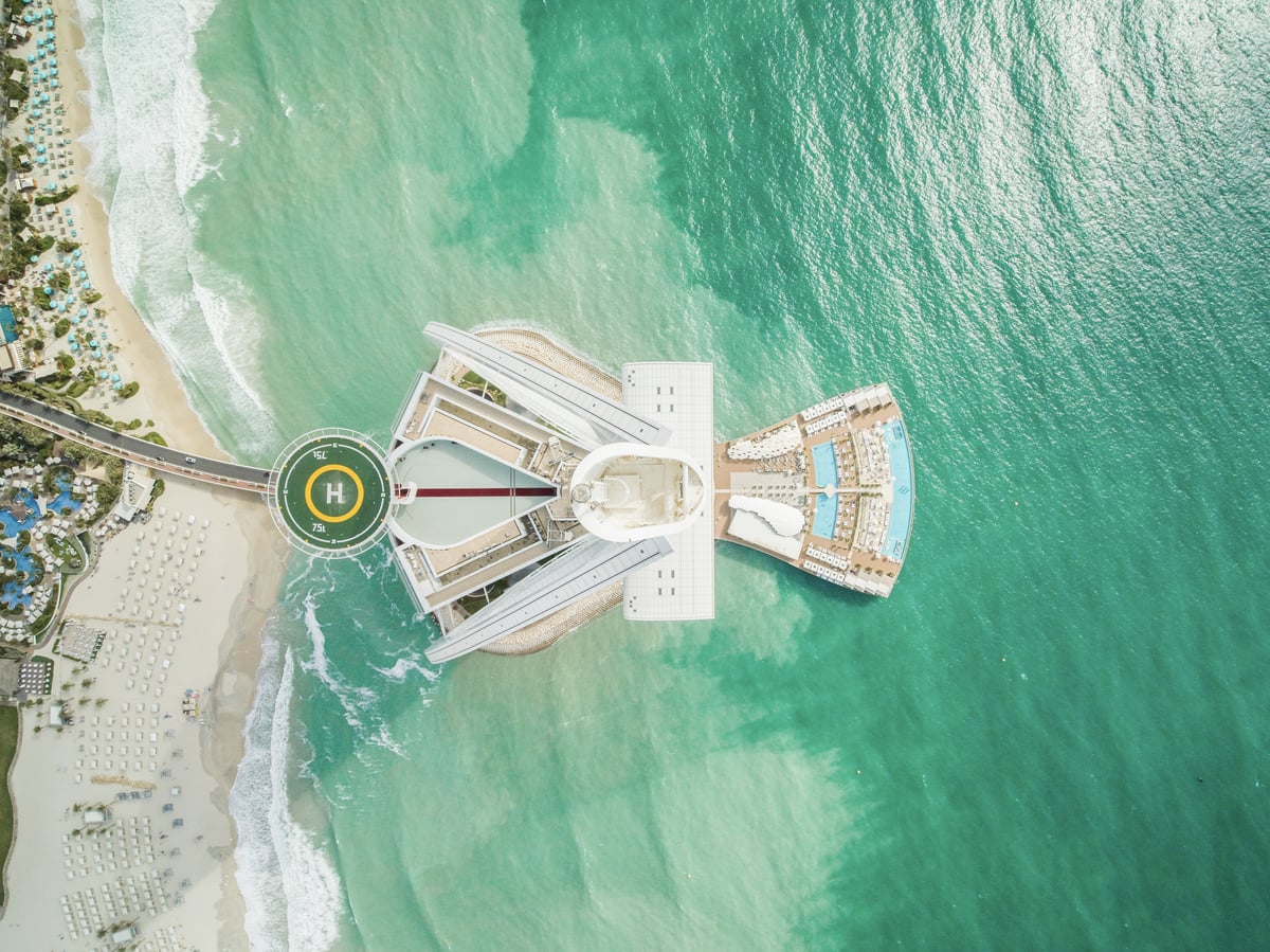 Top-down aerial view of Burj Al Arab's helipad, sail and island set in green-blue sea