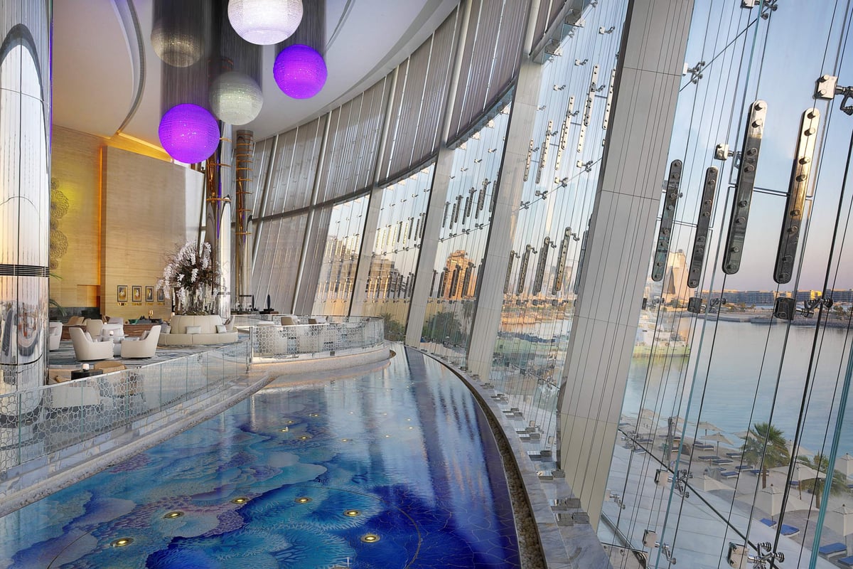 A long mosaic water channel beside lounge seating under glass globe lights, with full-height windows over the city at Conrad Abu Dhabi Etihad Towers.