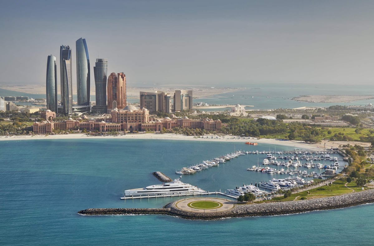 Aerial view of the marina, a superyacht and the long pink facade of Emirates Palace, with Abu Dhabi towers beyond.