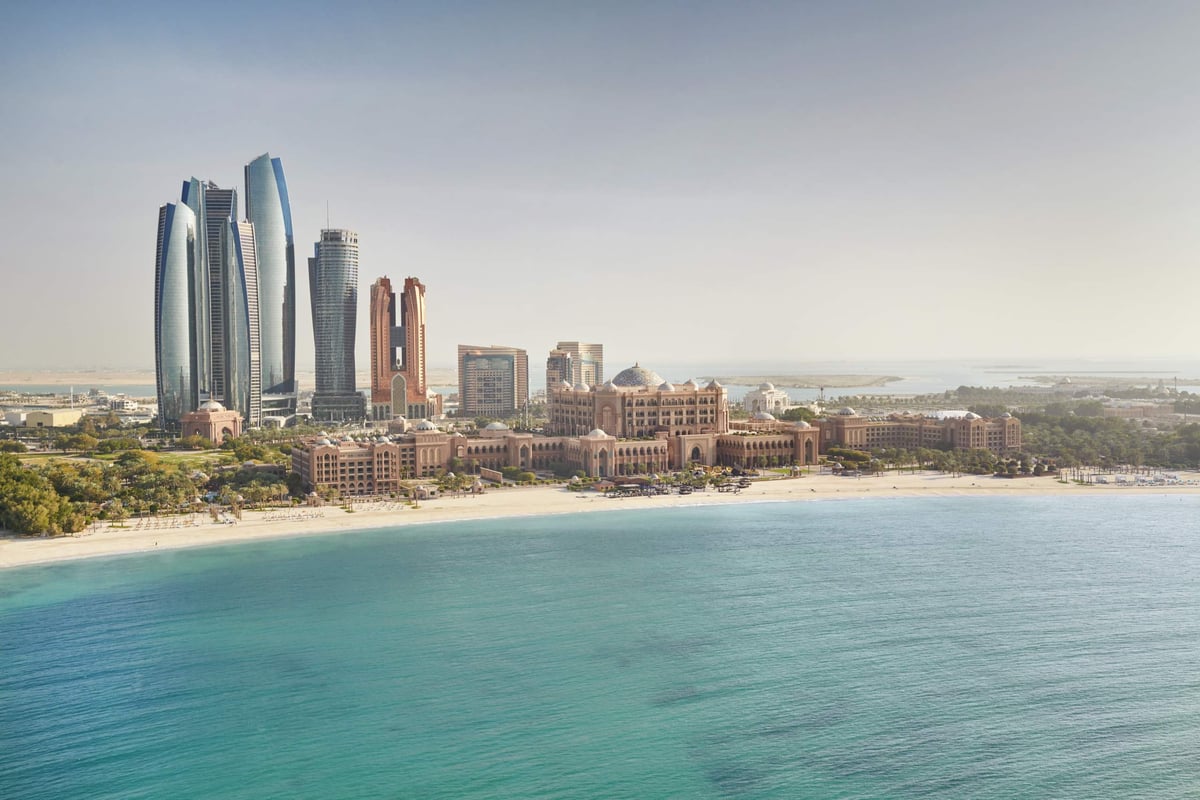 Emirates Palace Mandarin Oriental spreads along a white beach and turquoise water, with the Etihad Towers and Abu Dhabi skyline behind.