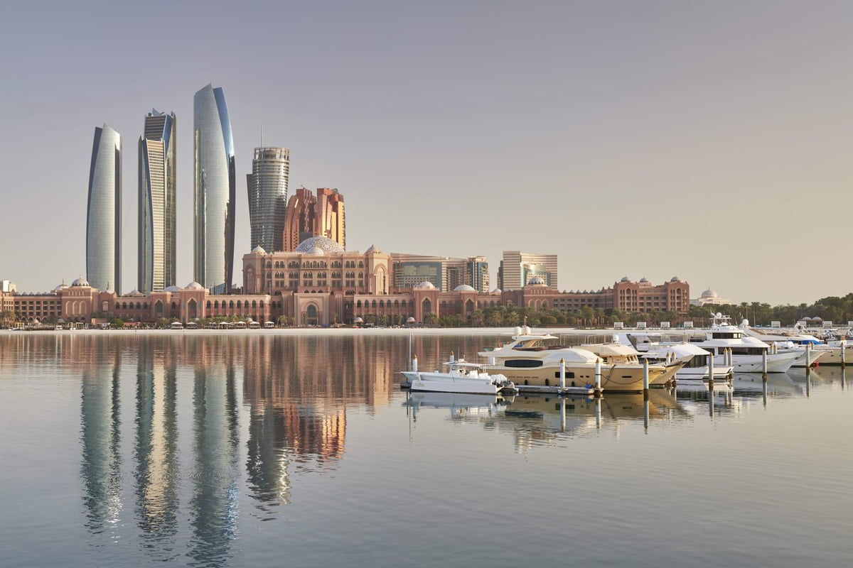 Yachts moored in the marina in front of Emirates Palace, the skyline reflected in still morning water.