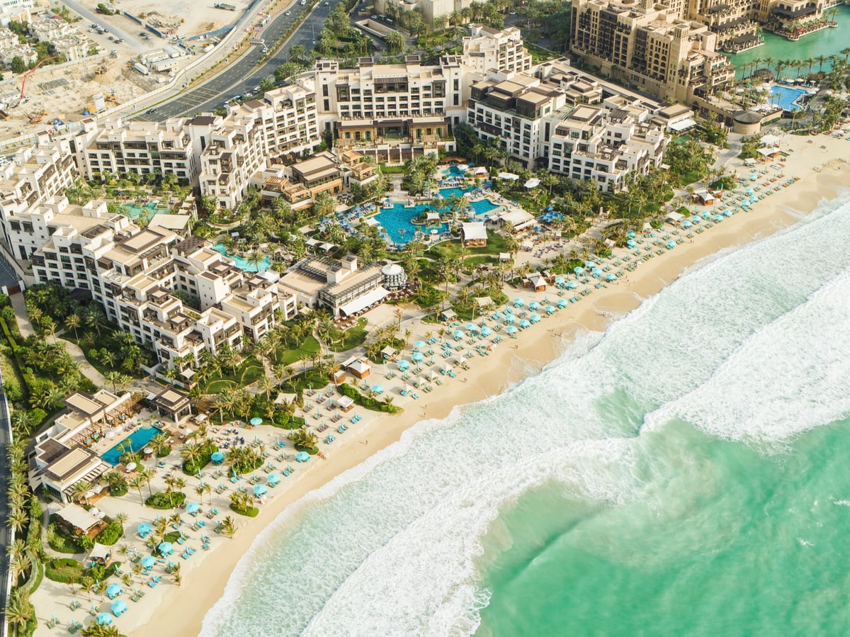 Aerial view of Jumeirah Al Naseem's low white buildings, pools and gardens above a wide sandy beach and turquoise sea.