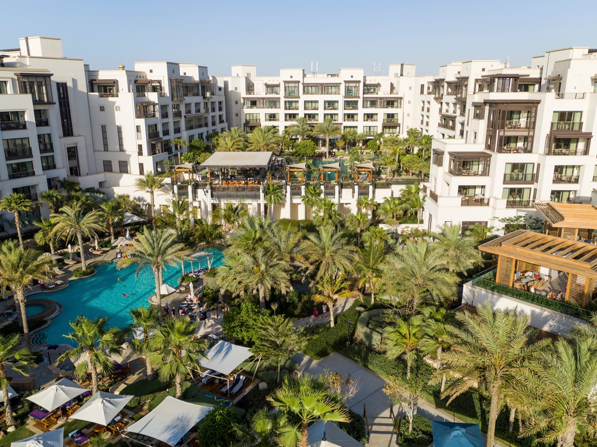 Drone view over the palm gardens and lagoon pool to the white guest wings of Jumeirah Al Naseem.