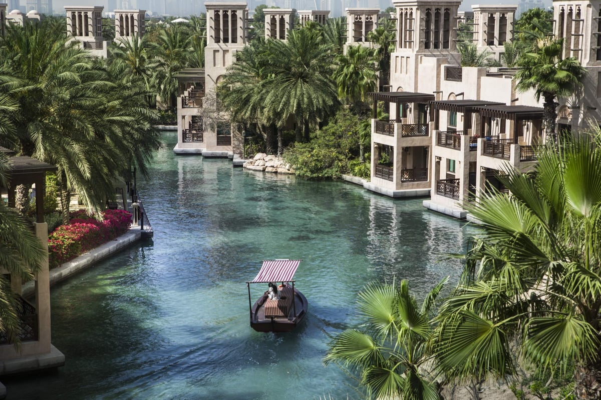 An abra glides along a palm-lined canal past the wind-tower buildings of Jumeirah Al Qasr.