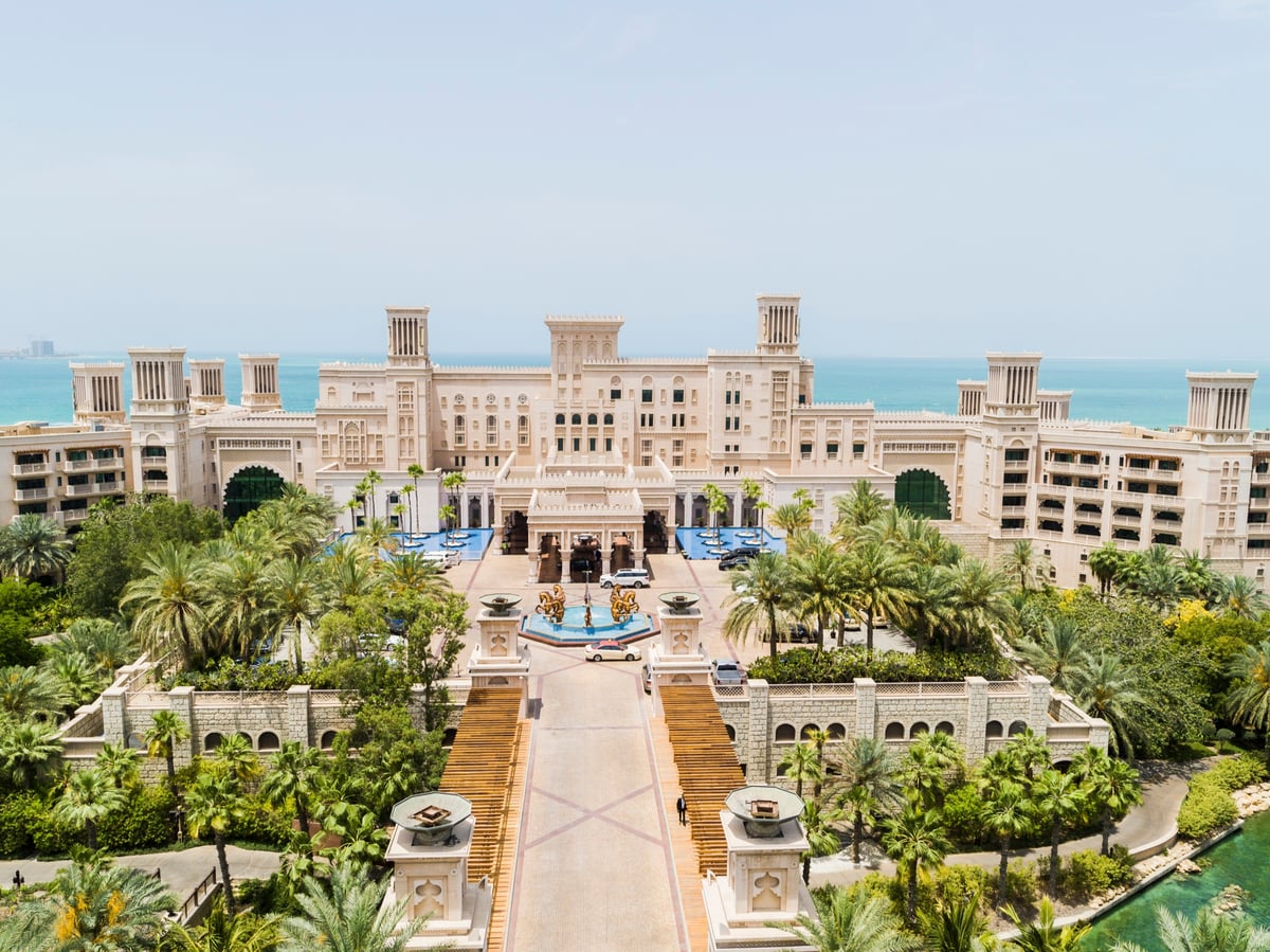 Aerial view of Jumeirah Al Qasr's palace facade, its grand stairway and gardens, with the Arabian Gulf behind.