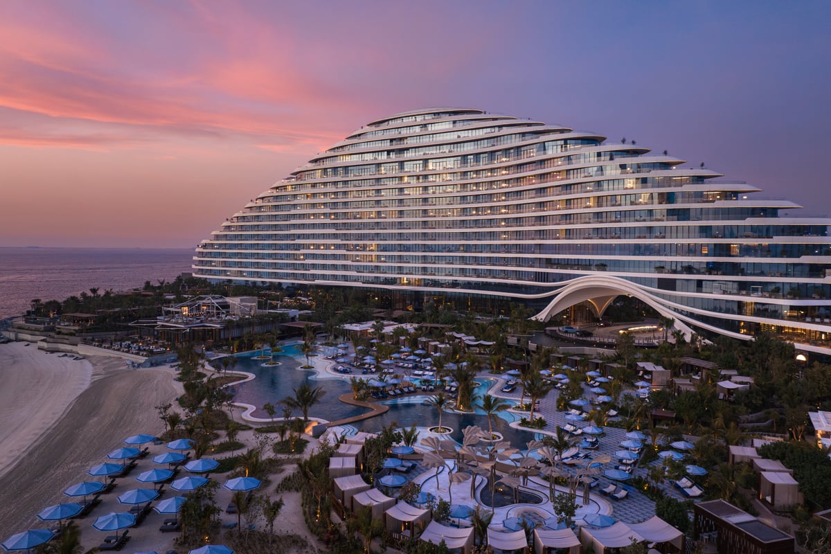 Aerial view of Jumeirah Marsa Al Arab at dusk, its curved terraced façade rising above the pools and beach