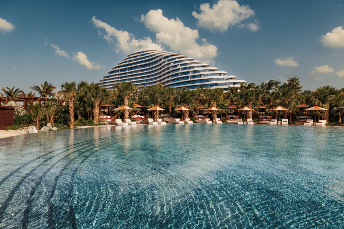 A long infinity pool lined with umbrellas, the hotel's curved façade beyond the palms