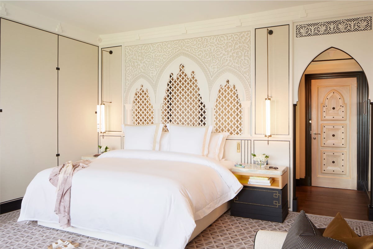Ocean Deluxe, king bed under a carved lattice headboard beside an arched wooden door, at Jumeirah Mina A'Salam.