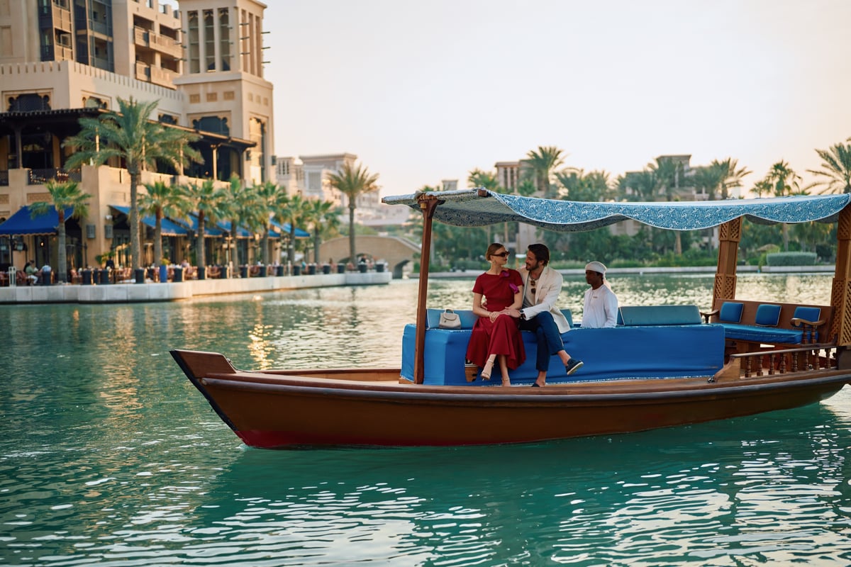 A couple sits in a blue-canopied abra steered by a boatman along the waterway past Jumeirah Mina A'Salam.