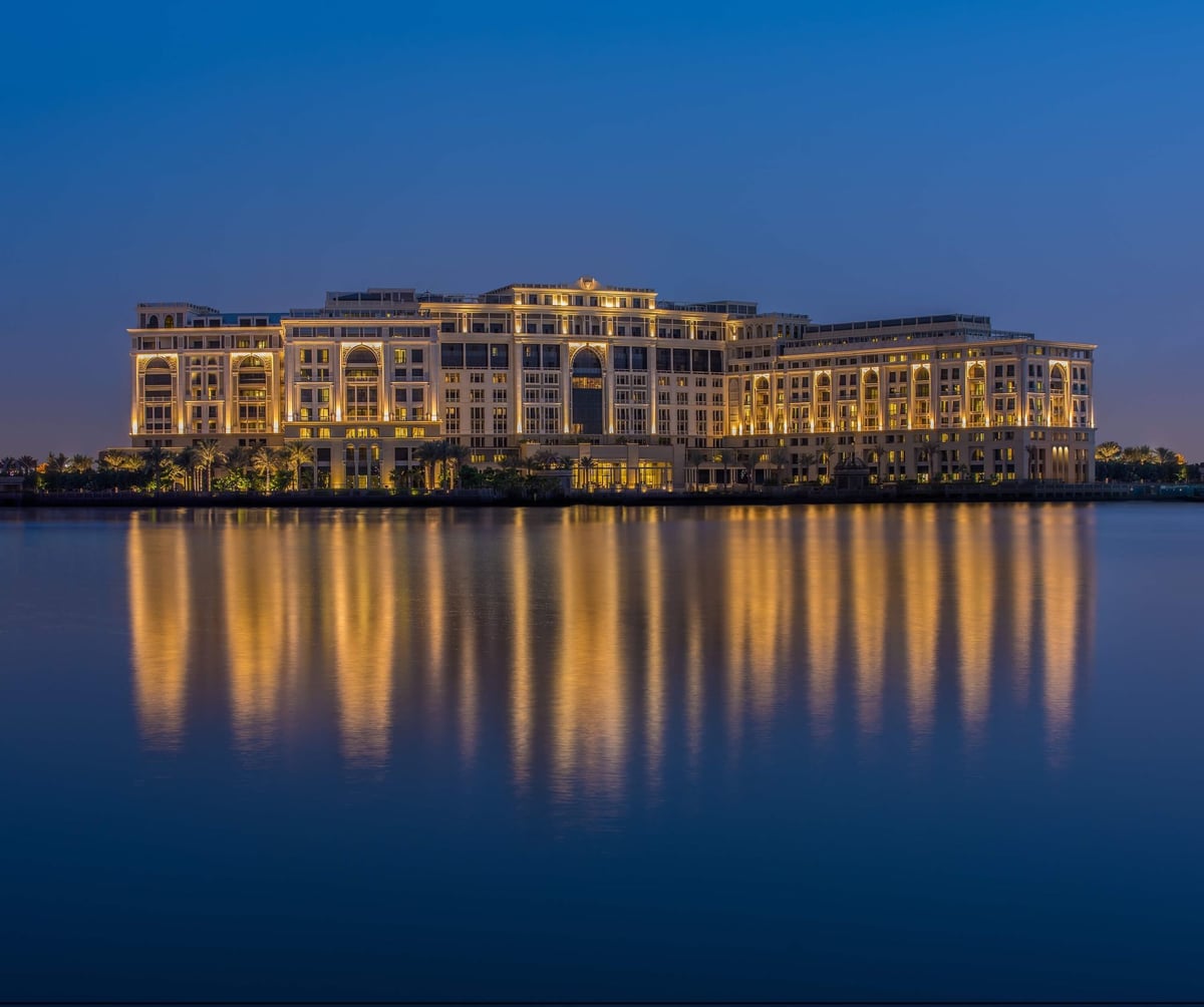 Palazzo Versace Dubai lit at dusk, its palace façade reflected in Dubai Creek