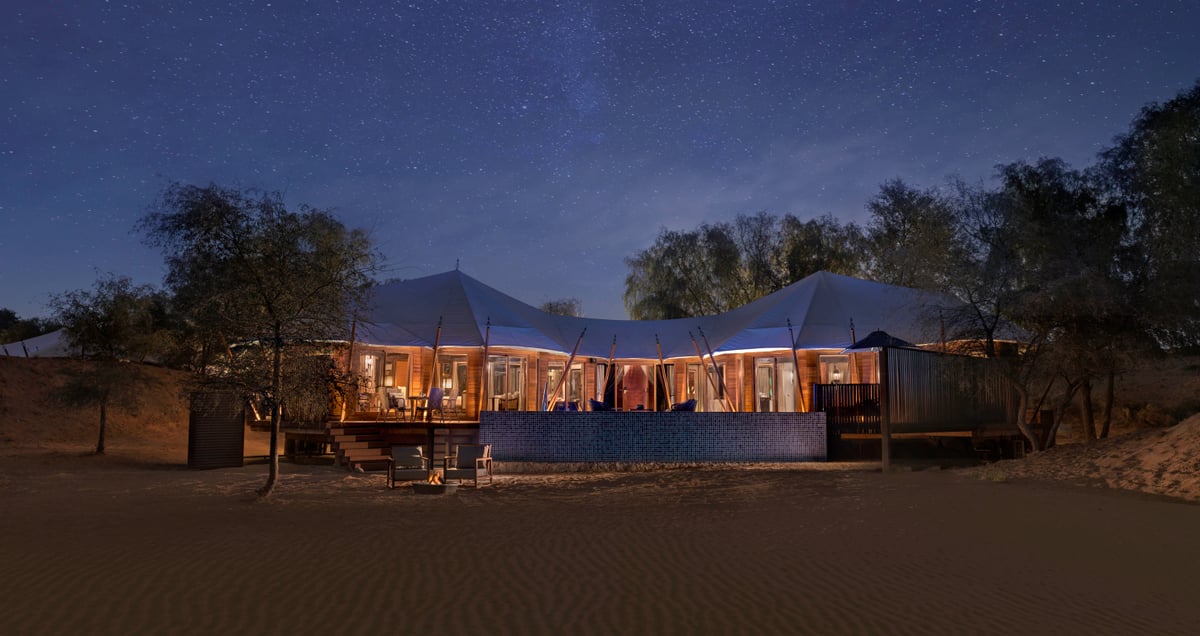 A tented villa lit from inside under a starry night sky in the desert at The Ritz-Carlton Al Wadi Desert.