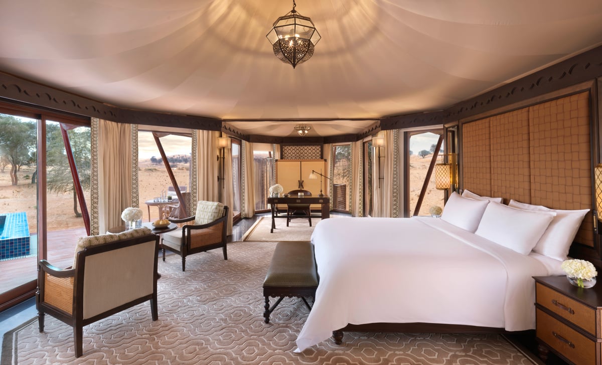 Al Khaimah Villa, king bed under a tented ceiling with armchairs and windows to the desert, at The Ritz-Carlton Al Wadi Desert.