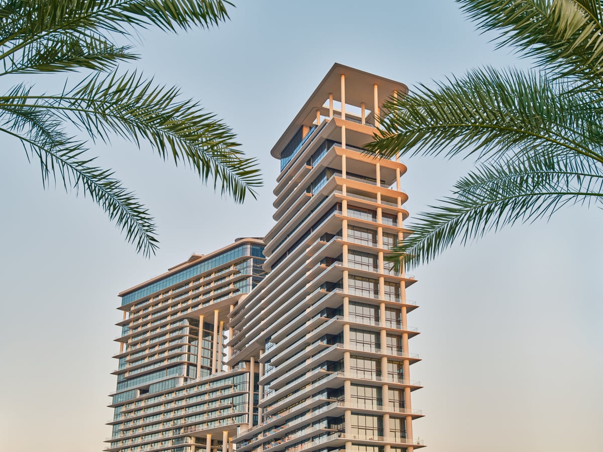 The stepped tower of The Lana seen from below between palm fronds under a clear sky.