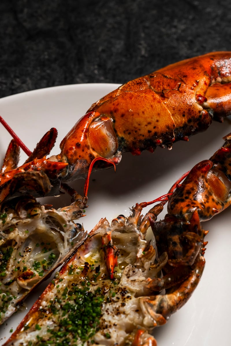 Two halves of a chargrilled lobster dressed with herbs and butter on a white plate