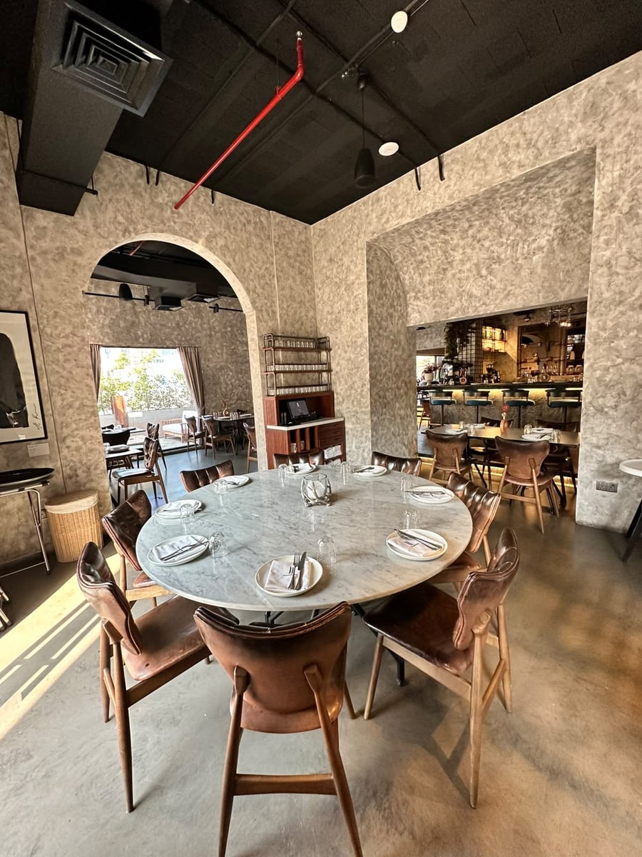 A round marble table laid for eight with leather chairs, stone arches opening onto the bar beyond