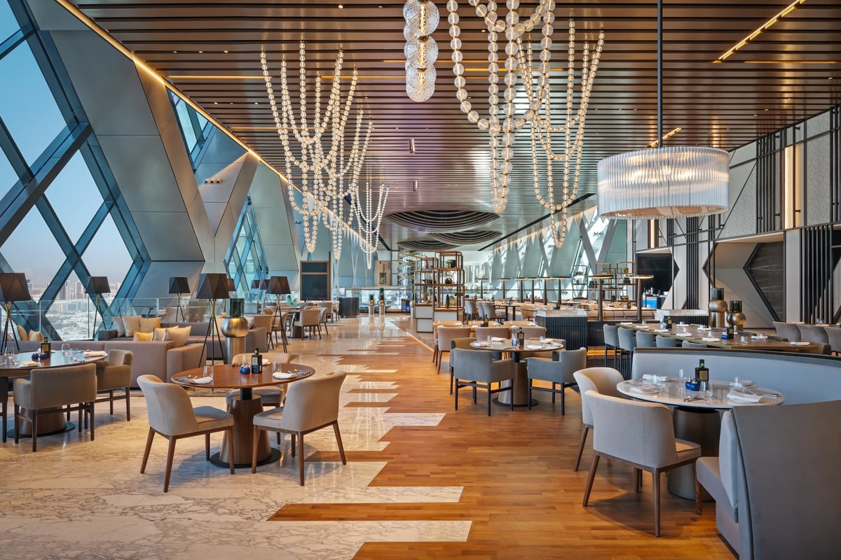 Aelia's long dining room beneath cascading strands of crystal, the building's diagonal glass frame and city views along one side