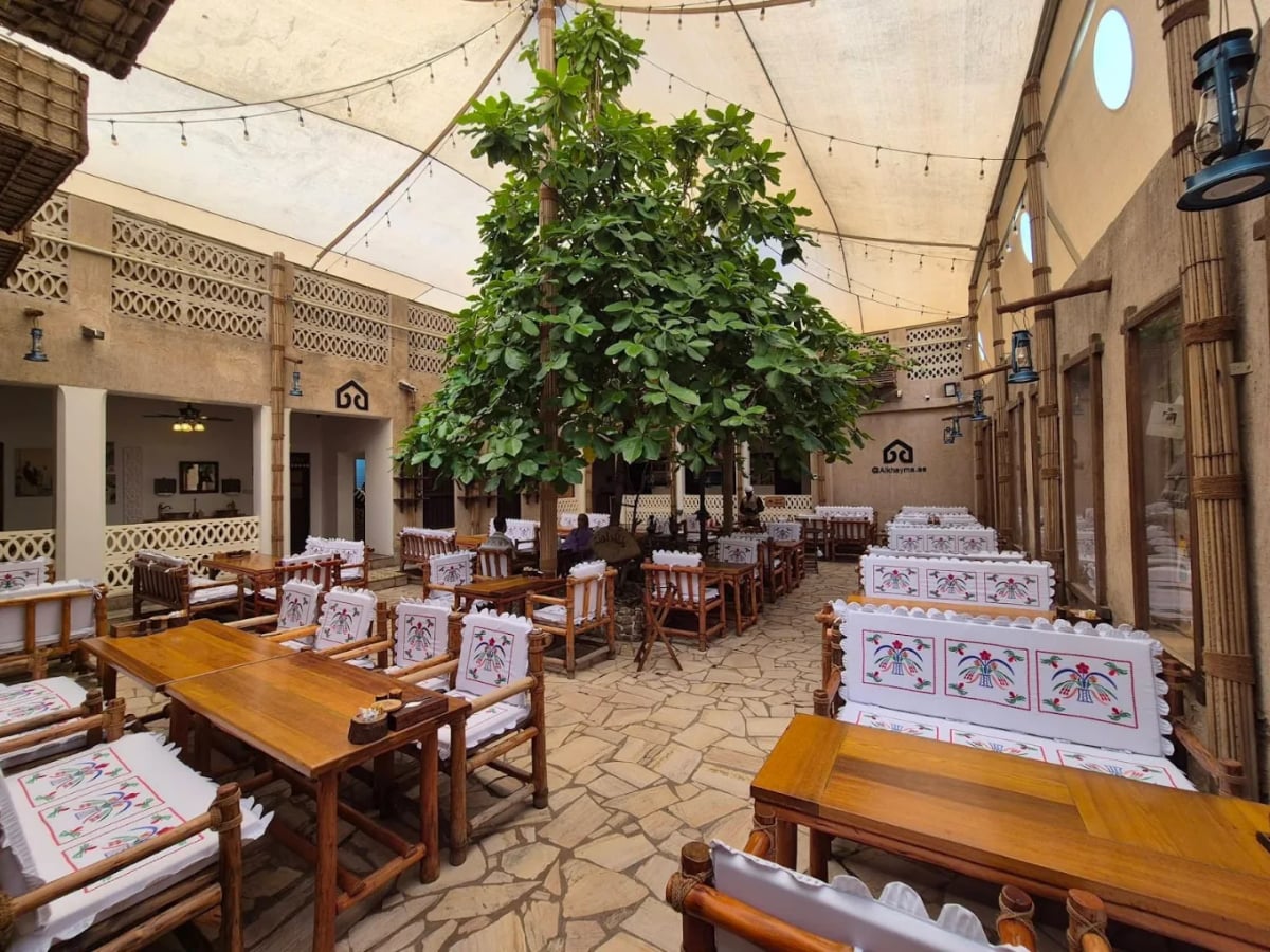 Wooden tables and benches with embroidered cushions around a large tree in a canopied courtyard