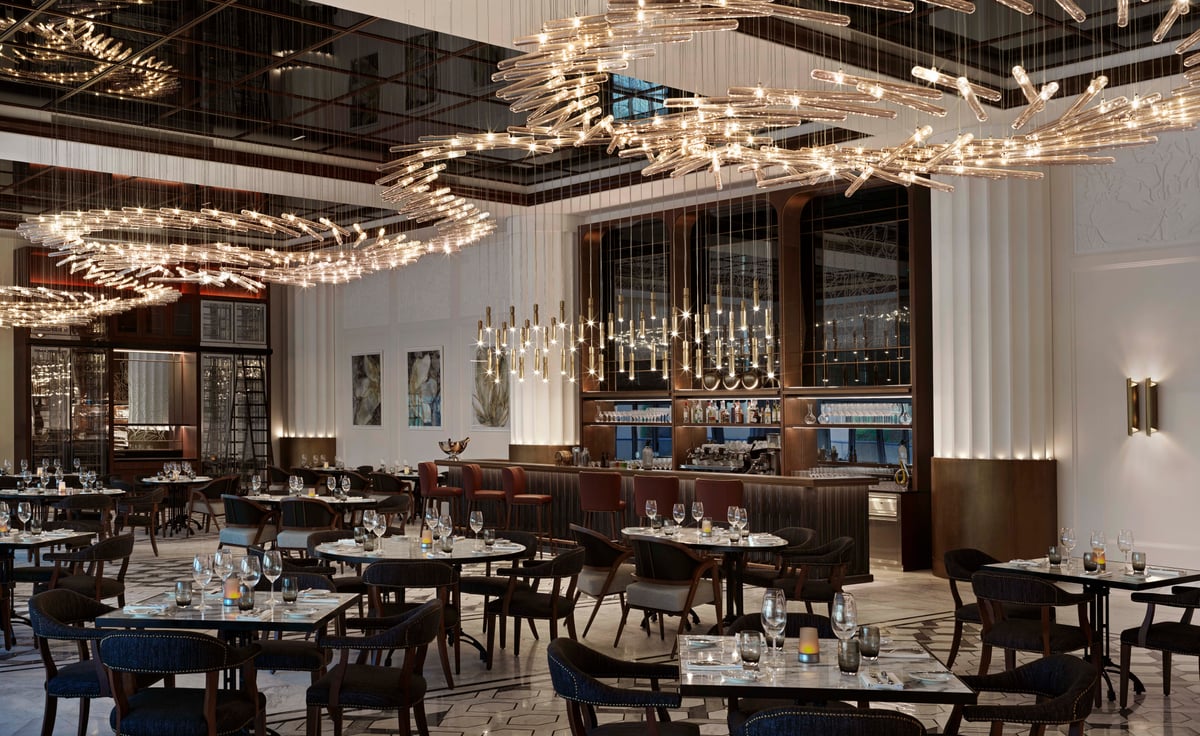 The main dining room's dark tables and chairs under looping chandeliers, a wine wall at the far end