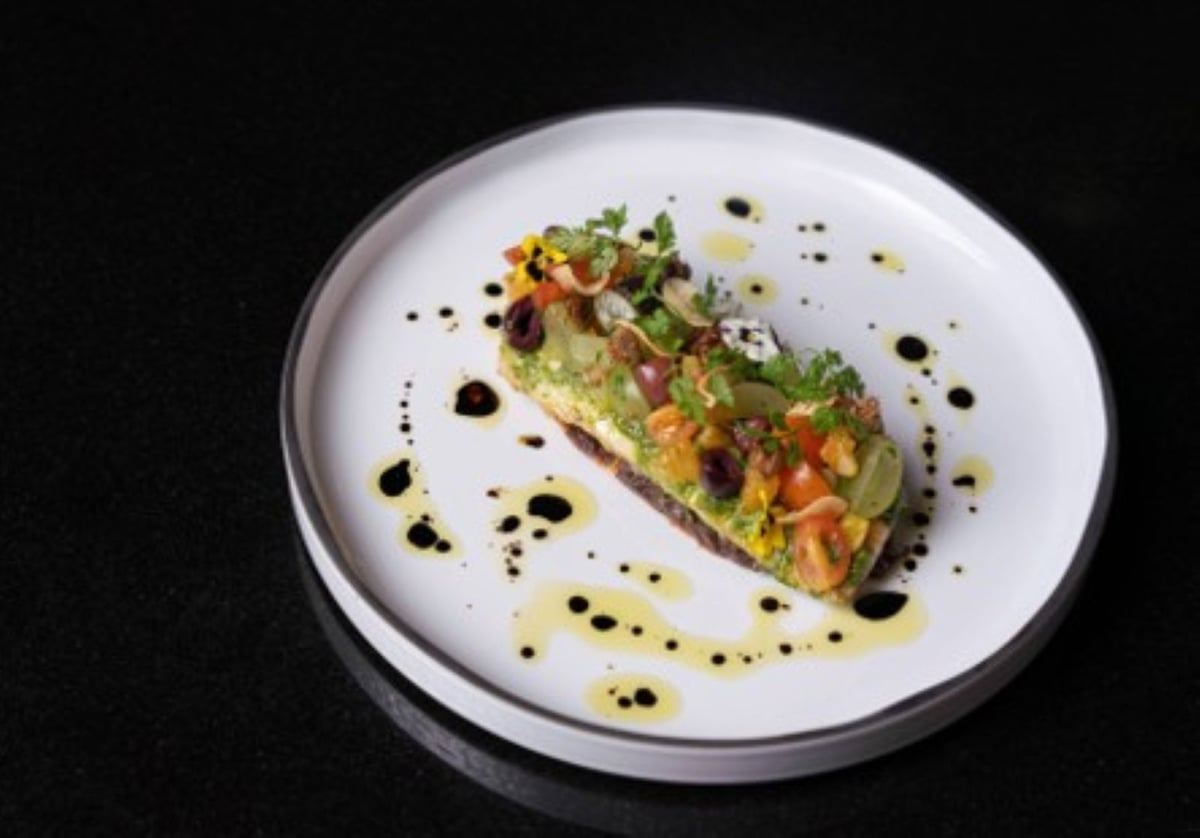 A plated starter of avocado and diced vegetables with herbs, dotted with olive oil and balsamic on a white plate