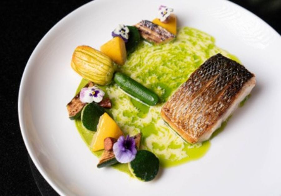 Crisp-skinned fish on a green herb risotto with baby vegetables and edible flowers