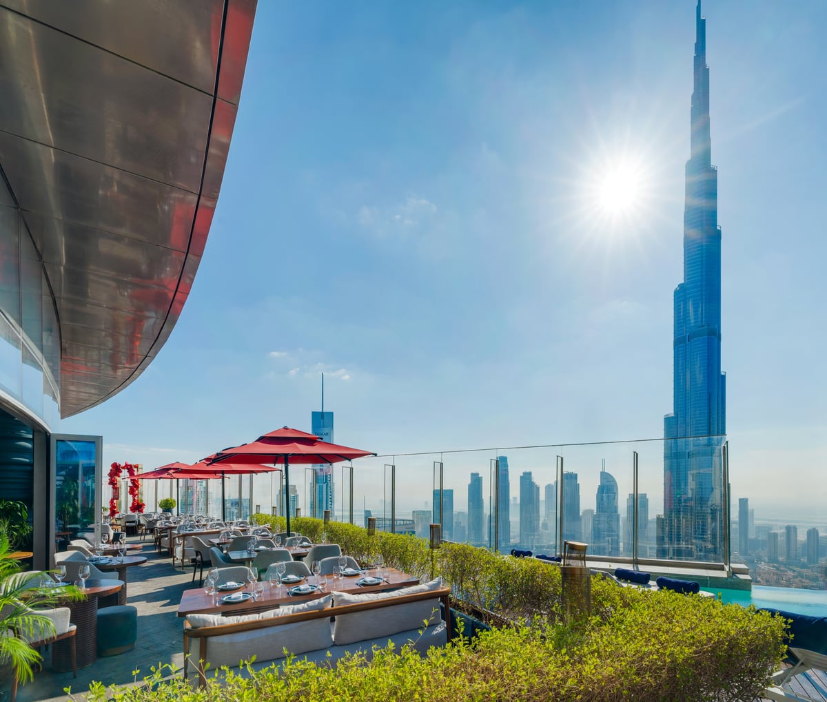 Red parasols and planting along the terrace edge in bright sun, the Burj Khalifa rising alongside