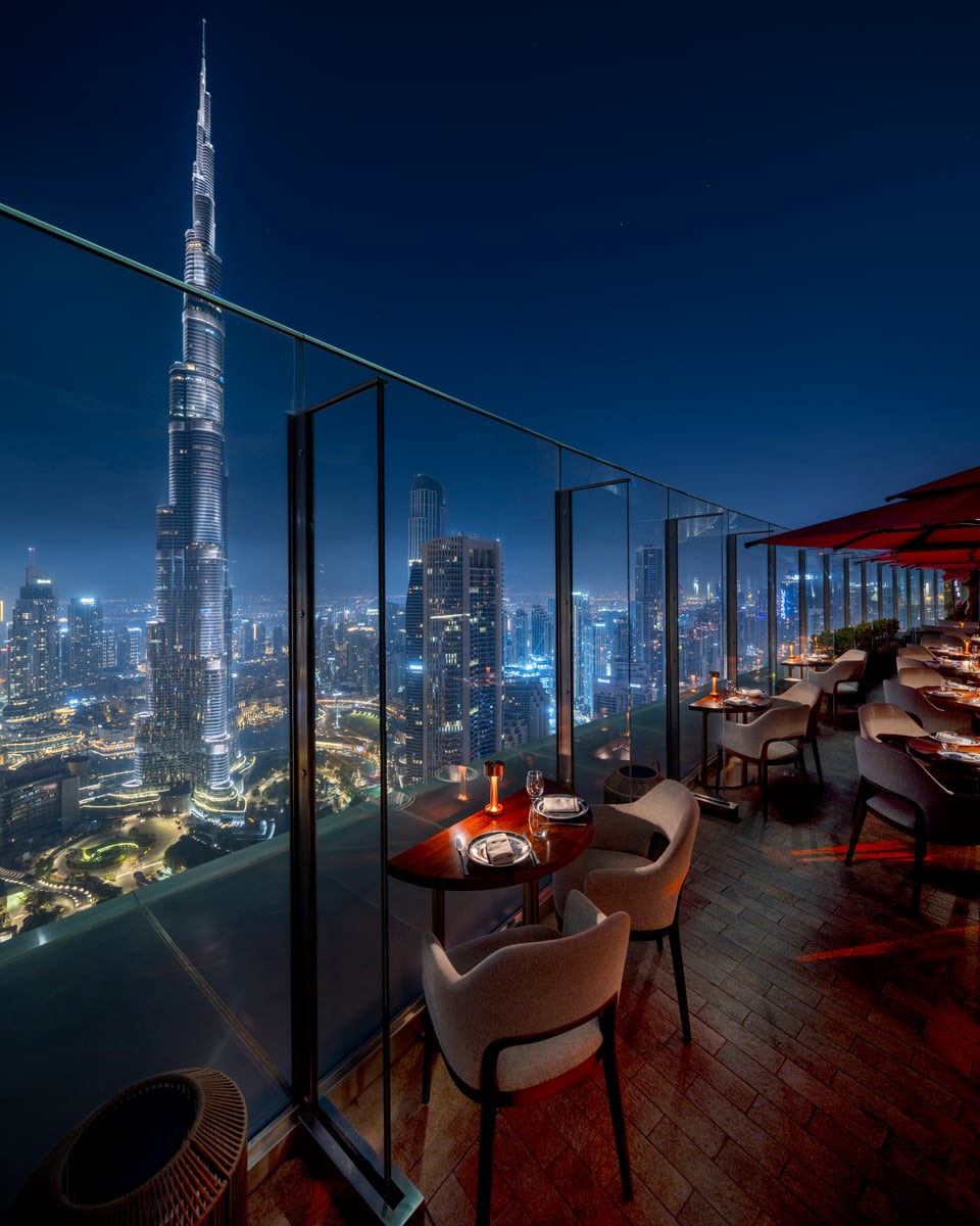 Terrace tables lit by small lamps along a glass balustrade, the illuminated Burj Khalifa and Downtown towers beyond