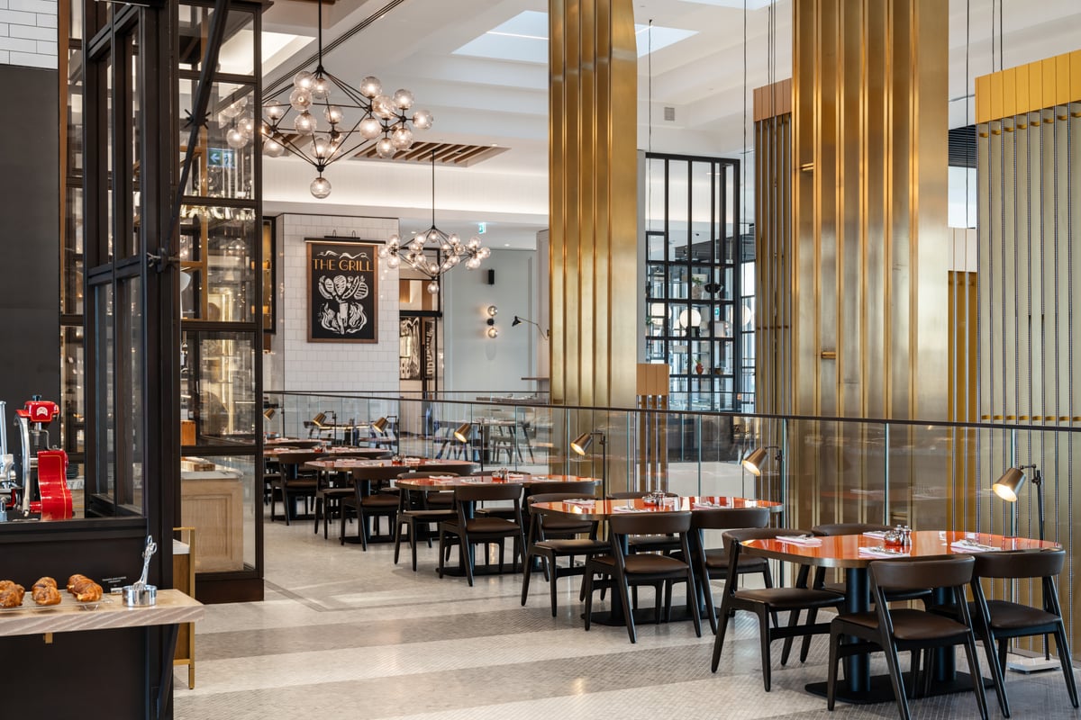 Tables with red tops and dark chairs between fluted gold columns, glass globe chandeliers above
