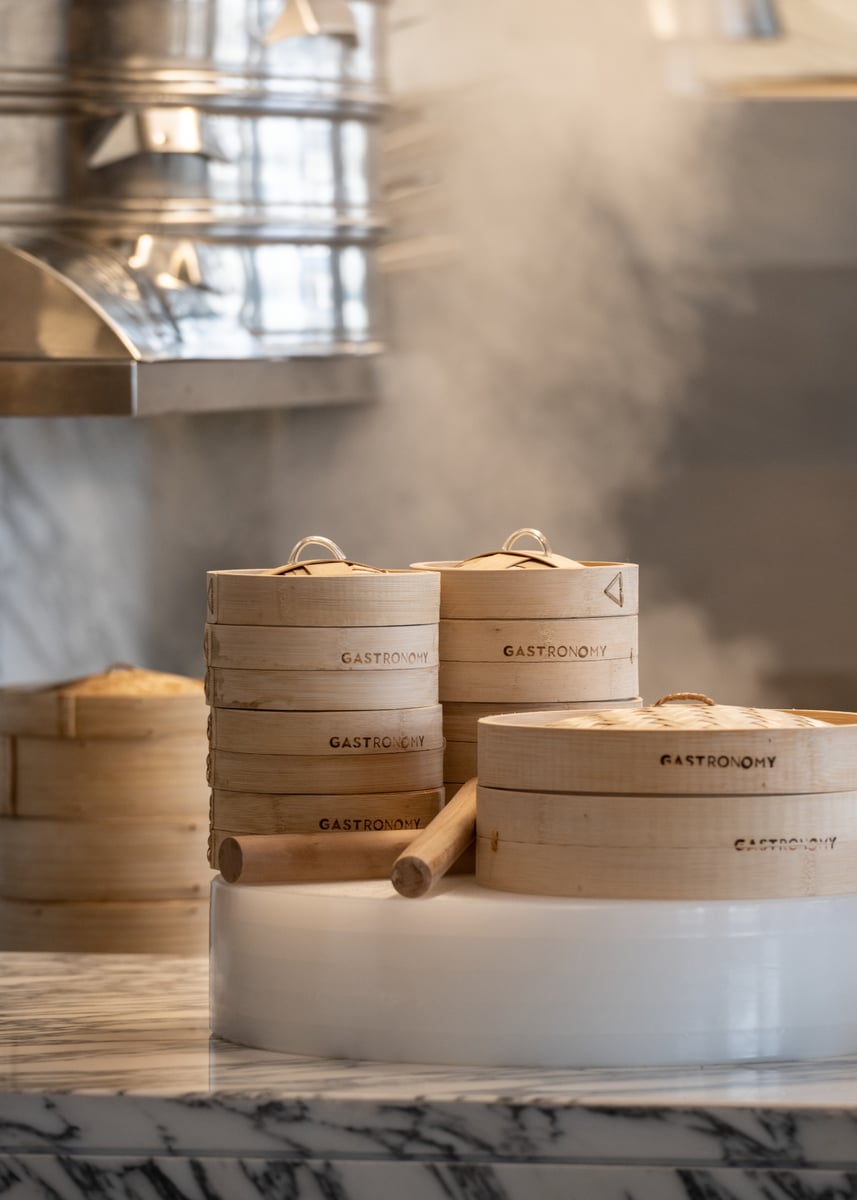 Stacked bamboo steamers releasing steam on a marble counter