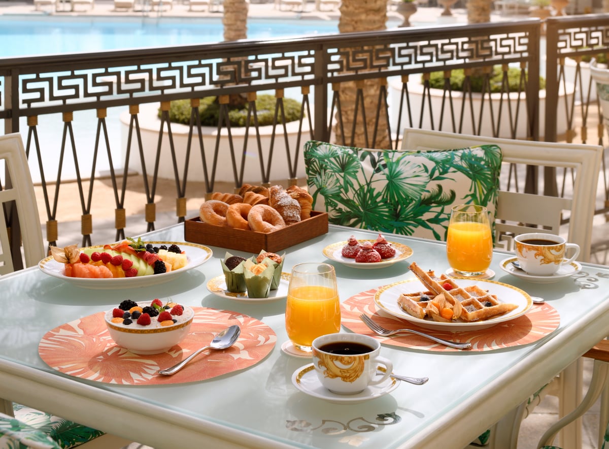 Breakfast laid on a terrace table: pastries, fruit, waffles, orange juice and Versace-patterned china