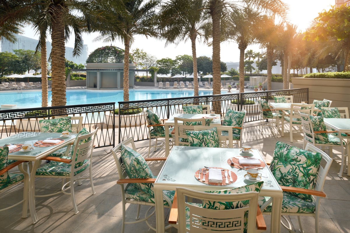 Terrace tables with palm-print cushions beside a Greek-key railing, the palm-lined pool glowing in late sun