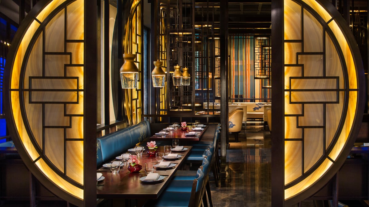 A long table with blue banquettes seen between two glowing round lattice screens